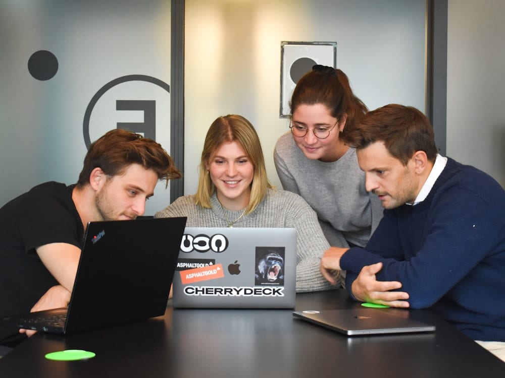 Four people working together around a laptop in an office