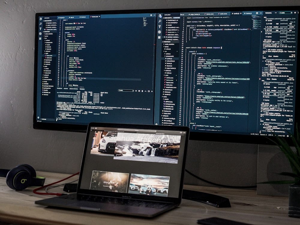 A laptop and a wide monitor showing code on a desk